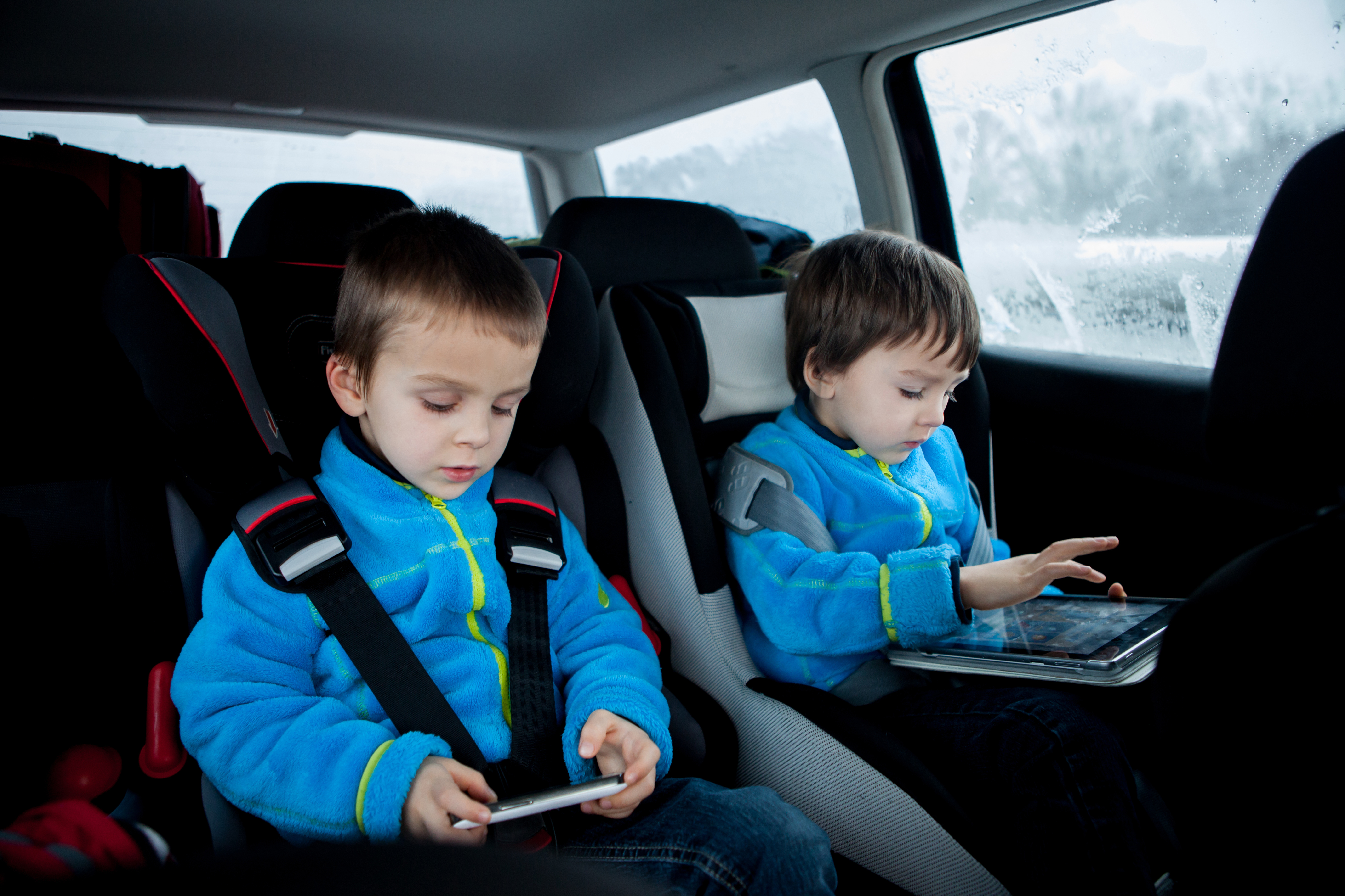Two kids in car seats, traveling in car, playing