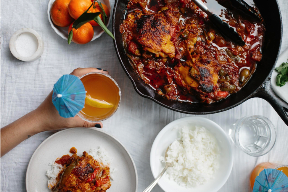 Pollo guisado and rice on a table with hand reaching out and holding citrus rum spritzer